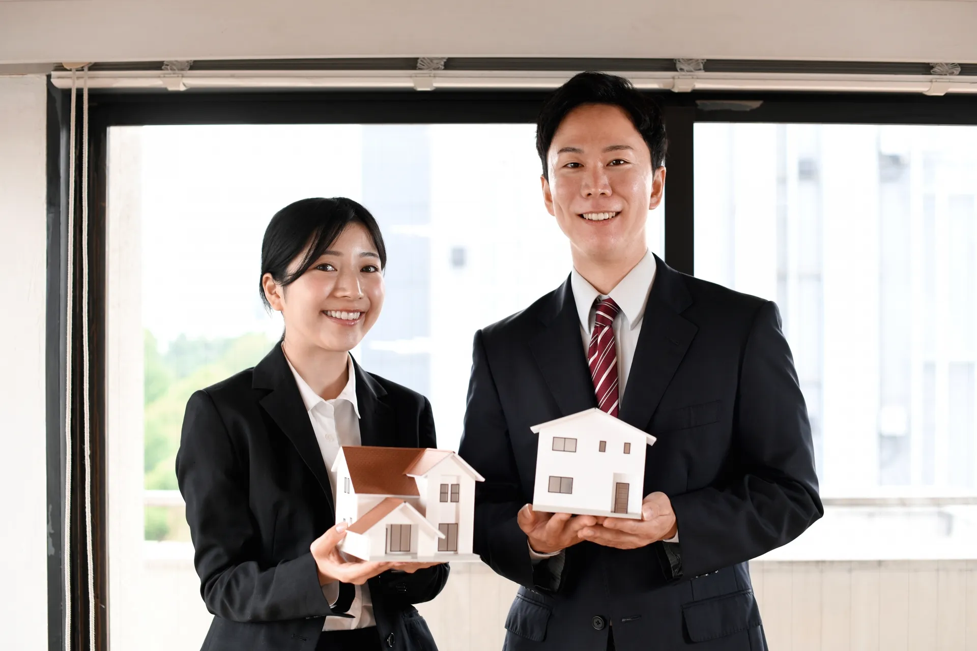 家の模型を持っているスーツの男女